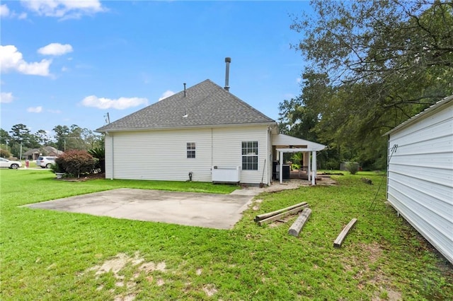 rear view of property featuring a shingled roof, a lawn, and a patio