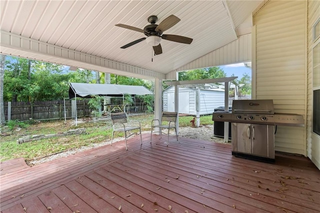 deck with an outbuilding, grilling area, a storage shed, a ceiling fan, and fence