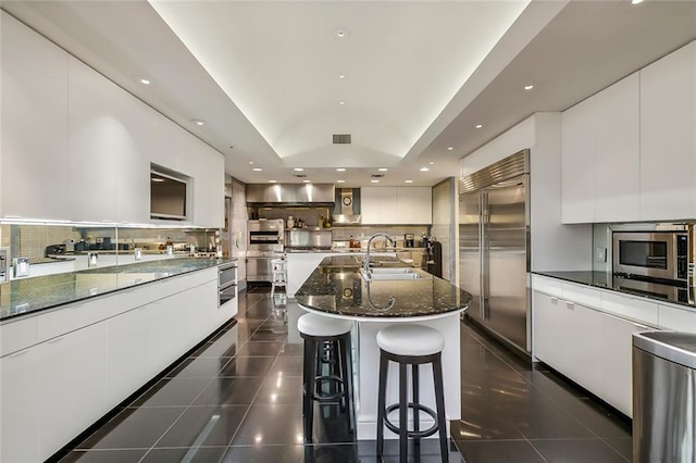 kitchen featuring modern cabinets, white cabinets, a sink, and built in appliances