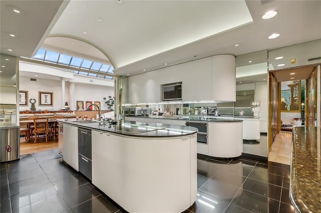 kitchen featuring a kitchen island with sink, dark countertops, modern cabinets, and white cabinetry