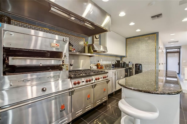 kitchen with visible vents, backsplash, white cabinetry, dark tile patterned floors, and wall chimney exhaust hood