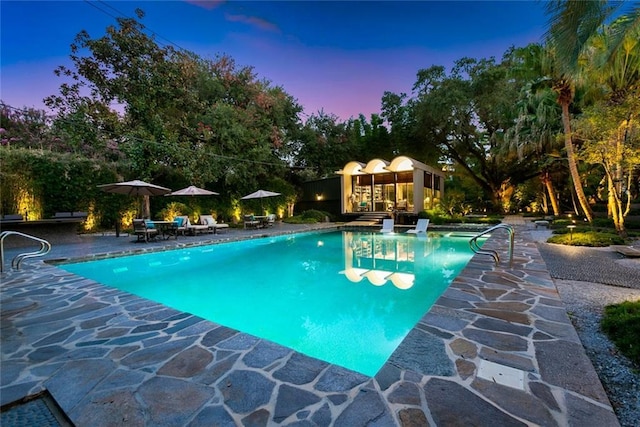 pool at dusk with a patio area and an outdoor pool