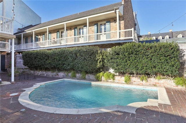 exterior space with brick siding, a balcony, and an outdoor pool