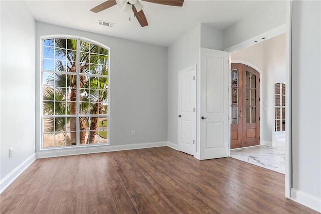 empty room featuring visible vents, wood finished floors, arched walkways, baseboards, and ceiling fan