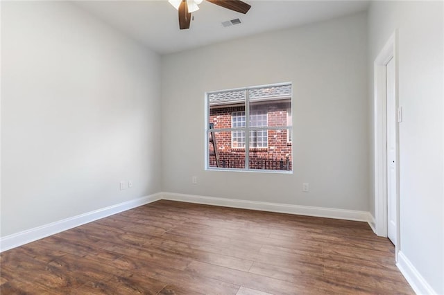 empty room with dark wood-style floors, visible vents, a ceiling fan, and baseboards