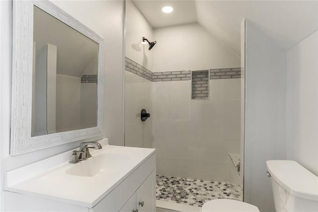 bathroom with a tile shower, toilet, vanity, and lofted ceiling