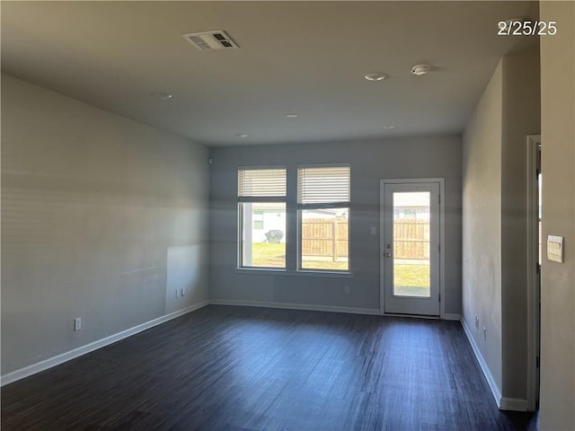 empty room with dark wood-type flooring, visible vents, and baseboards