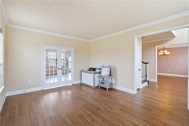 empty room with french doors, crown molding, an inviting chandelier, wood finished floors, and baseboards