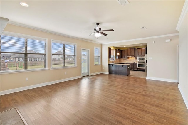 unfurnished living room with light wood-style flooring, baseboards, ceiling fan, and ornamental molding