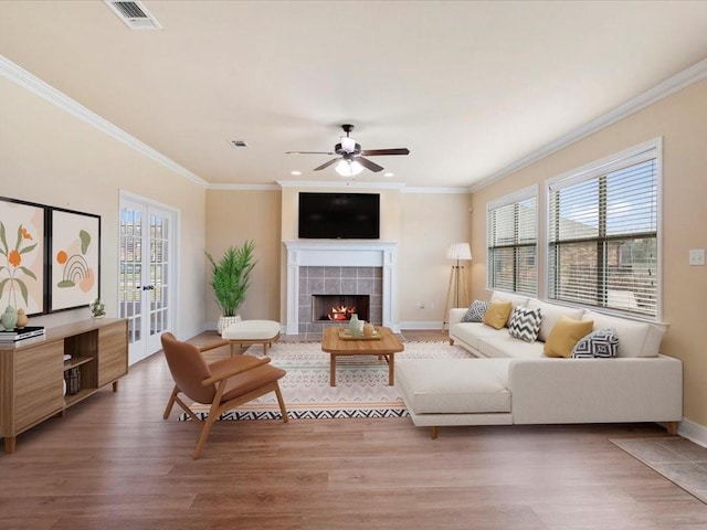 living room featuring a tile fireplace, visible vents, crown molding, and light wood-style flooring