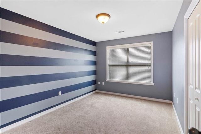 carpeted empty room featuring an accent wall, visible vents, and baseboards