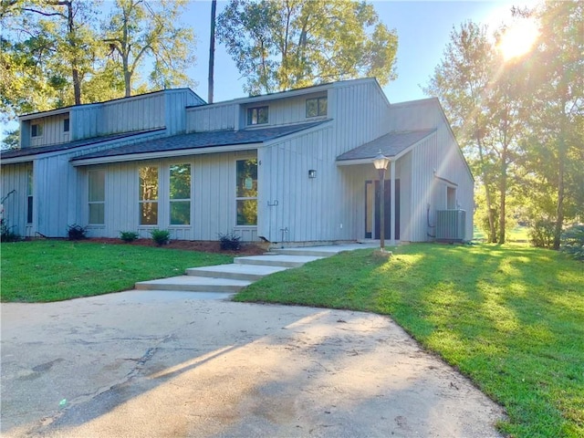 view of front facade featuring central AC unit, a front yard, and a shingled roof