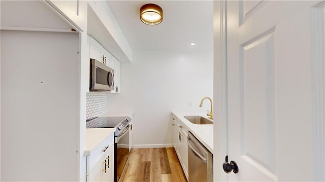 kitchen with light wood-style flooring, a sink, white cabinets, light countertops, and appliances with stainless steel finishes