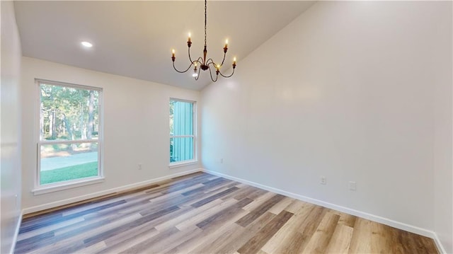 empty room with lofted ceiling, light wood-type flooring, a notable chandelier, and baseboards