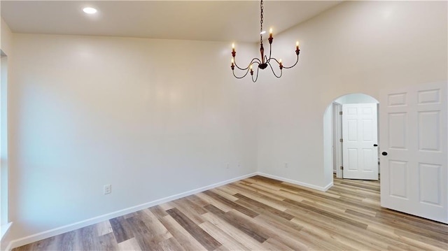 spare room with arched walkways, light wood-style flooring, recessed lighting, baseboards, and an inviting chandelier