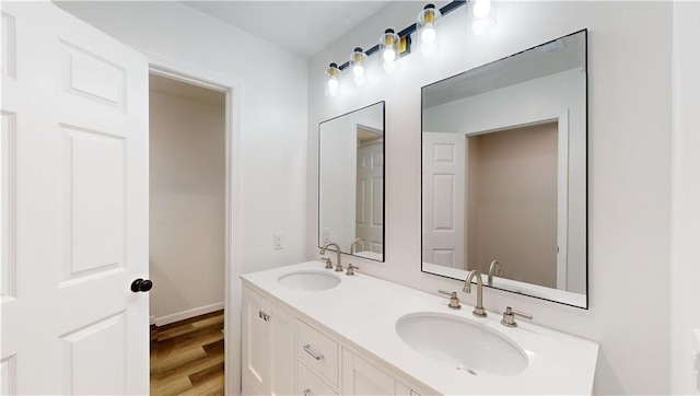 bathroom featuring double vanity, wood finished floors, a sink, and baseboards