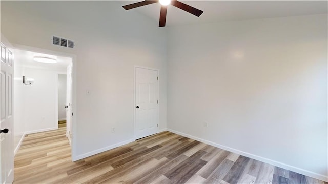 spare room with light wood finished floors, baseboards, visible vents, a towering ceiling, and ceiling fan