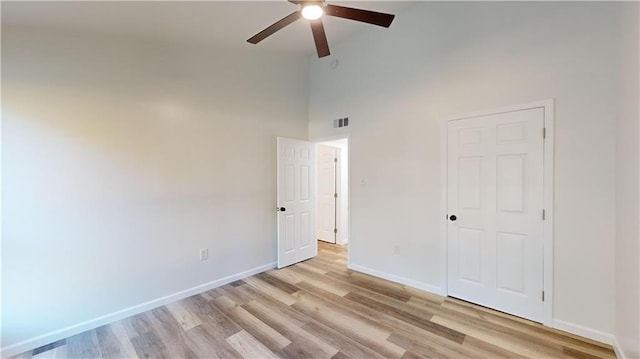 unfurnished bedroom with visible vents, baseboards, a ceiling fan, a towering ceiling, and light wood-style floors