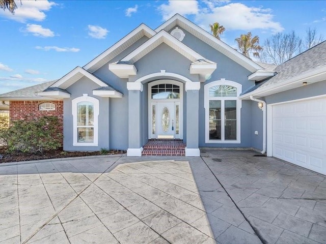 doorway to property featuring an attached garage, brick siding, and stucco siding