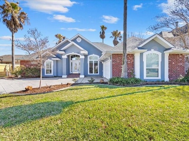 single story home with a garage, a front yard, brick siding, and stucco siding