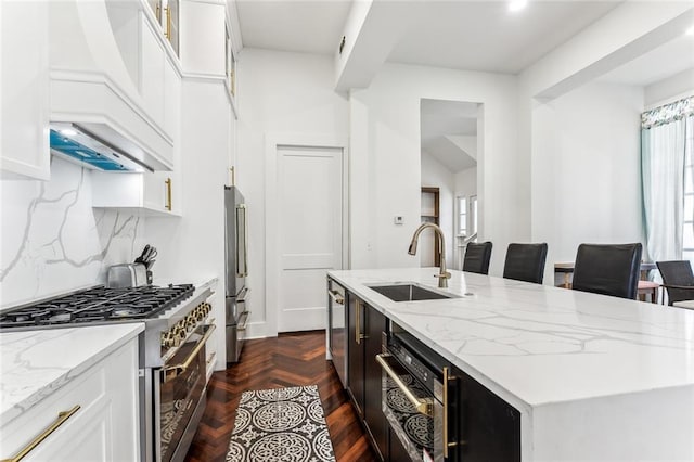 kitchen with premium appliances, an island with sink, a sink, and white cabinetry