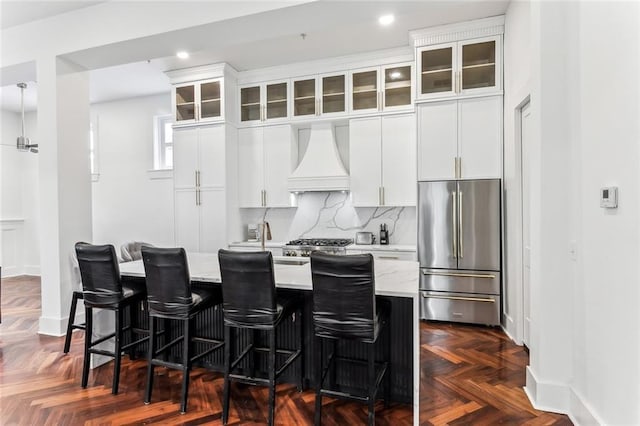 kitchen featuring custom exhaust hood, stainless steel fridge, glass insert cabinets, and white cabinets