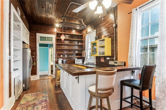 kitchen featuring wooden walls, a kitchen breakfast bar, freestanding refrigerator, open shelves, and dark wood finished floors