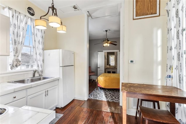 kitchen featuring white cabinets, freestanding refrigerator, light countertops, pendant lighting, and a sink