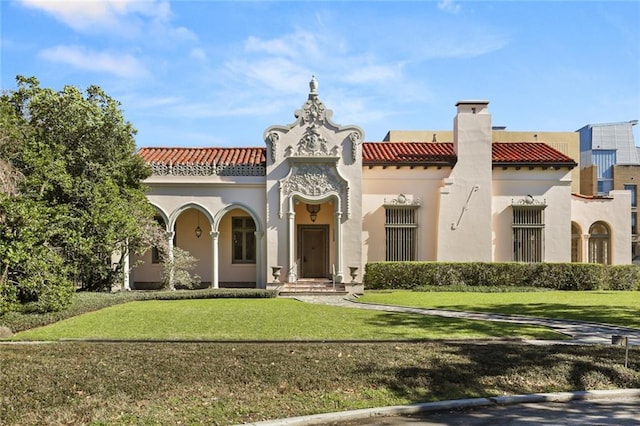 back of house with a chimney, a yard, a tiled roof, and stucco siding