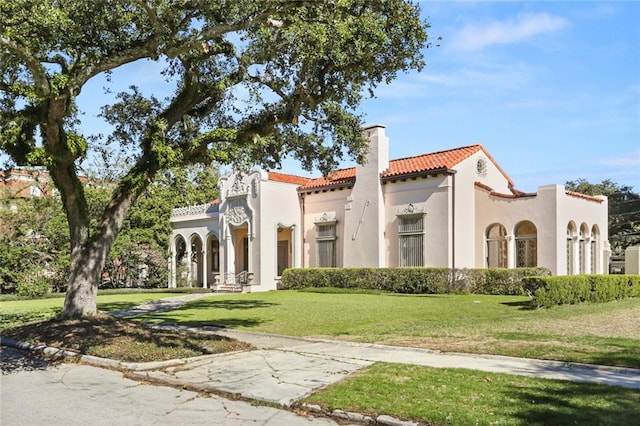 mediterranean / spanish home with a tile roof, a chimney, a front lawn, and stucco siding