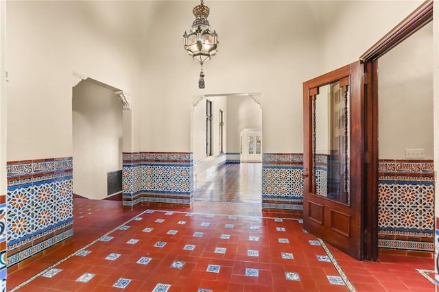 hallway with tile patterned flooring, a high ceiling, visible vents, and a notable chandelier