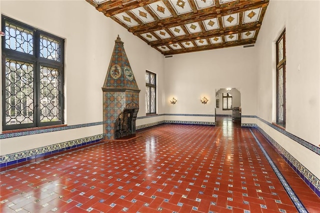 unfurnished living room with a towering ceiling, a fireplace, baseboards, and beam ceiling