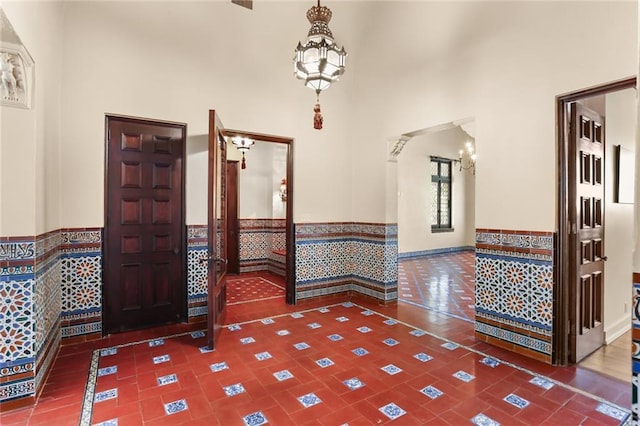 tiled entryway featuring a chandelier, a wainscoted wall, and a towering ceiling