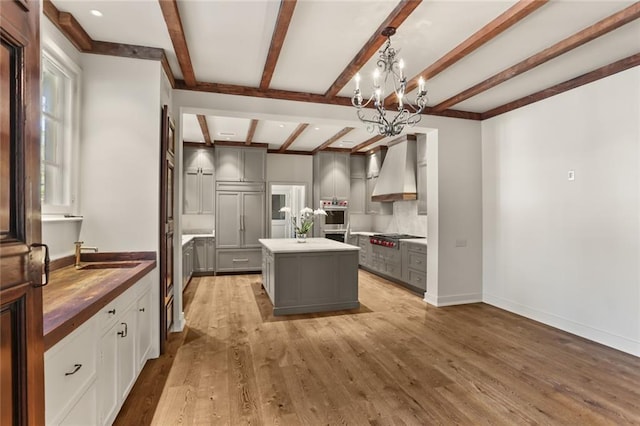 kitchen featuring light wood finished floors, a center island, gray cabinets, wall chimney range hood, and a sink