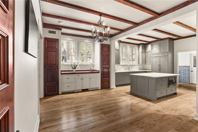 kitchen with gray cabinets, light countertops, light wood-style flooring, a chandelier, and paneled fridge