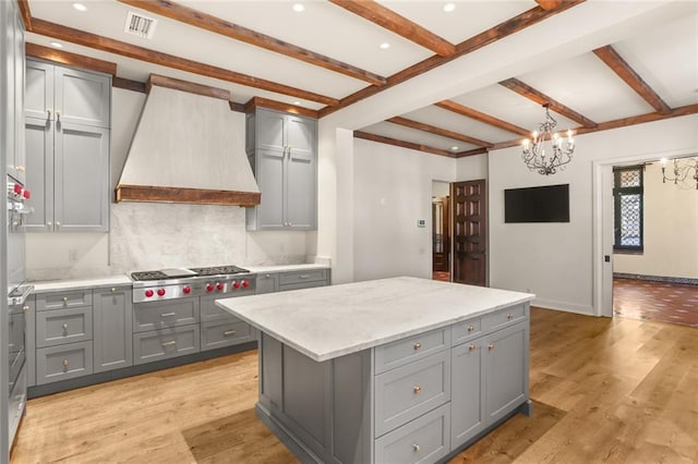 kitchen featuring custom range hood, gray cabinets, light wood-type flooring, stainless steel gas cooktop, and beam ceiling