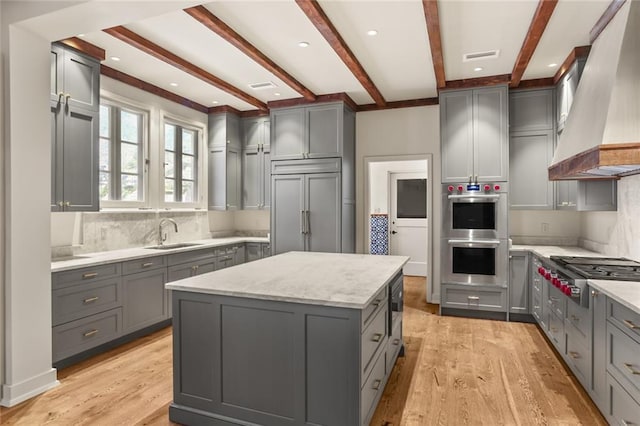 kitchen featuring built in refrigerator, gas stovetop, premium range hood, and gray cabinetry