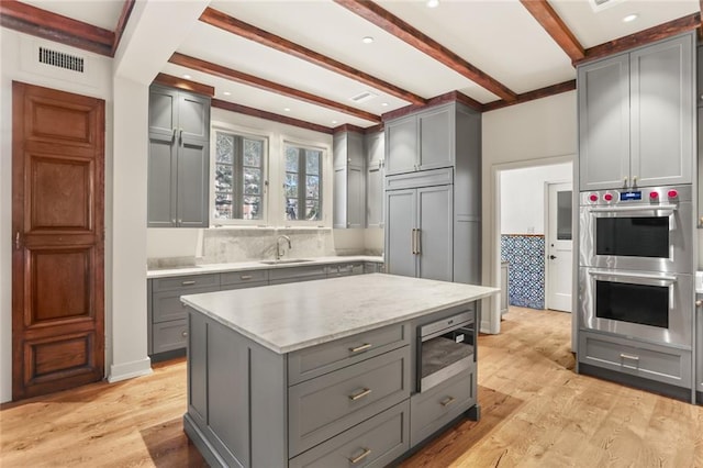 kitchen with light wood finished floors, gray cabinets, visible vents, a sink, and built in appliances