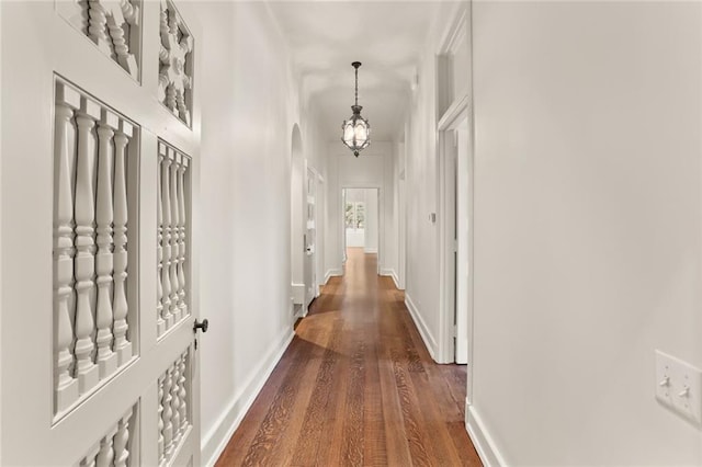 hall featuring arched walkways, dark wood-style flooring, an inviting chandelier, and baseboards