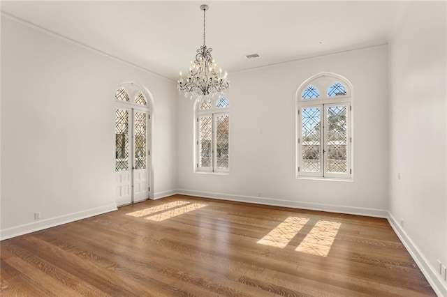 unfurnished dining area with visible vents, a notable chandelier, baseboards, and wood finished floors