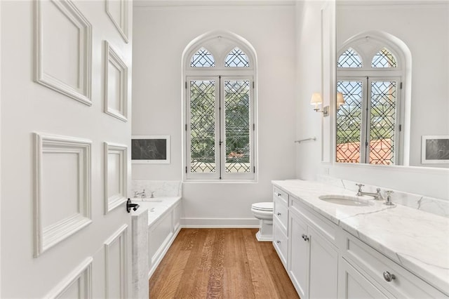 bathroom with baseboards, toilet, wood finished floors, vanity, and a bath