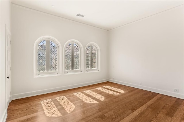 empty room with baseboards, crown molding, visible vents, and wood finished floors