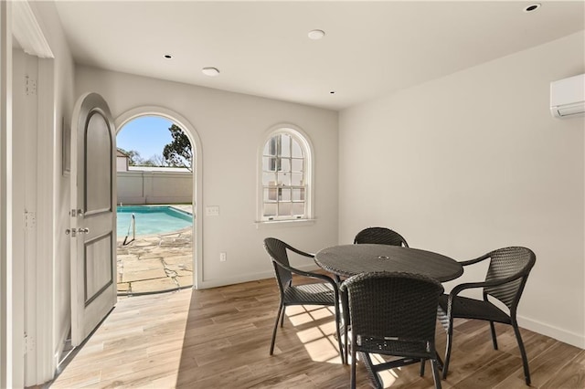 dining space featuring baseboards, a wall mounted air conditioner, and light wood finished floors