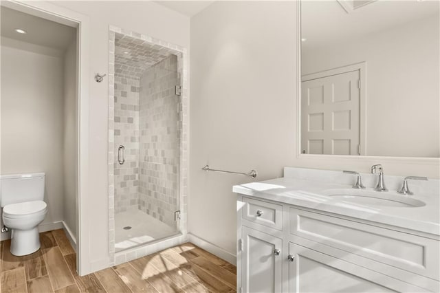 full bath featuring toilet, wood finish floors, vanity, baseboards, and a stall shower