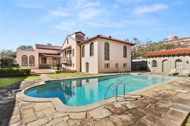 rear view of house with a tiled roof, stucco siding, a patio area, and an outdoor pool