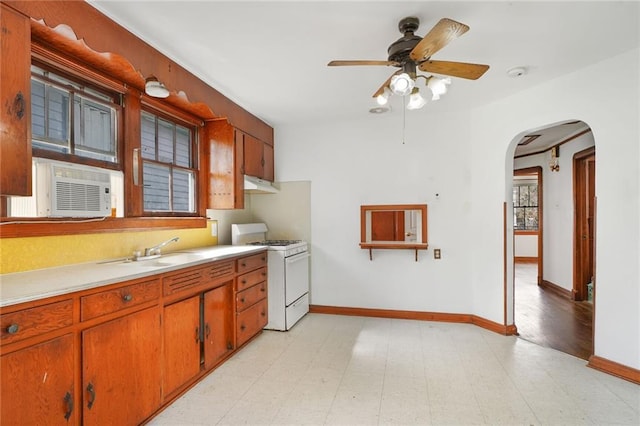 kitchen featuring white range with gas cooktop, arched walkways, light countertops, under cabinet range hood, and a sink