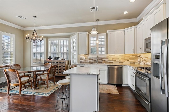 kitchen featuring decorative light fixtures, appliances with stainless steel finishes, white cabinets, a kitchen island, and a sink