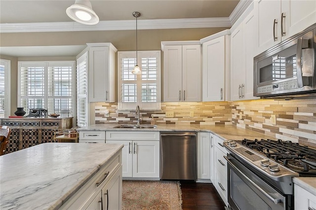 kitchen featuring appliances with stainless steel finishes, ornamental molding, white cabinets, a sink, and light stone countertops