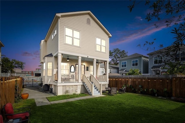 back of house at dusk featuring a yard, a porch, stairway, and a fenced backyard