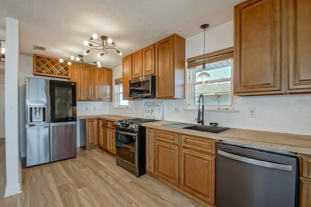 kitchen featuring a sink, light countertops, appliances with stainless steel finishes, brown cabinetry, and decorative light fixtures